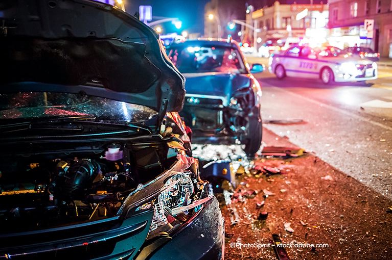 Two cars are parked on the right side of the road. An SUV appears to have rear-ended another car. The car that has been rear-ended has its hood open and its headlights shattered. Its rear bumper appears to have fallen off.