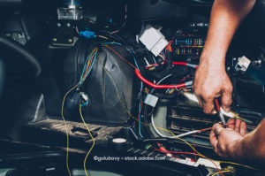 A mechanic (only the hands are visible) is cutting a red wire. Several wires and even certain electrical parts are exposed.