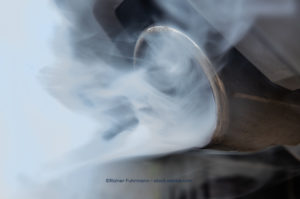 Close up of a tail pipe with visible exhaust gases leaking out in white smoke.