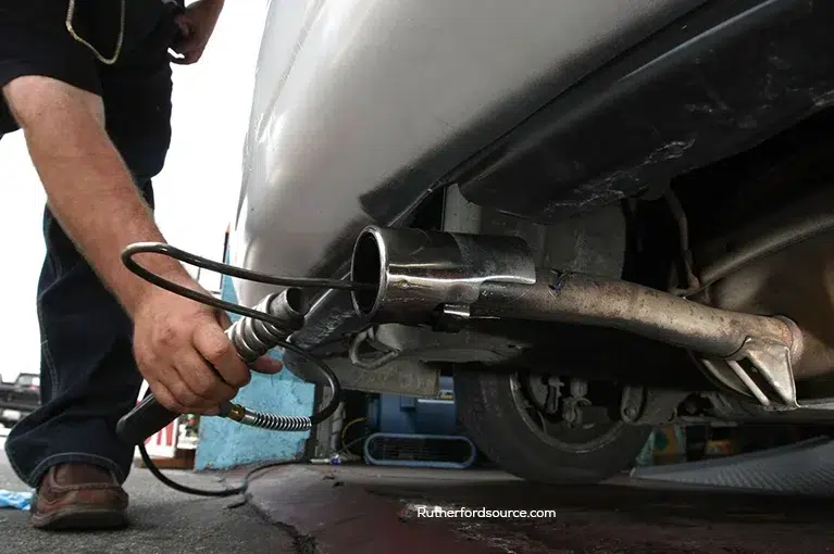 A mechanic inserts a tool into the tailpipe of a car.