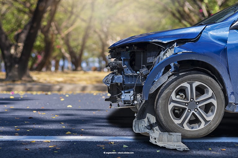 A blue car's front bumper and headlights are destroyed, exposing interior components.