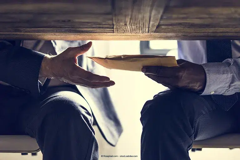 A close-up of one man handing another man a manila envelope under the table.