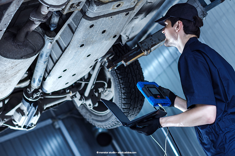 A mechanic uses an OBD scanner and a laptop to diagnose a vehicle issue.