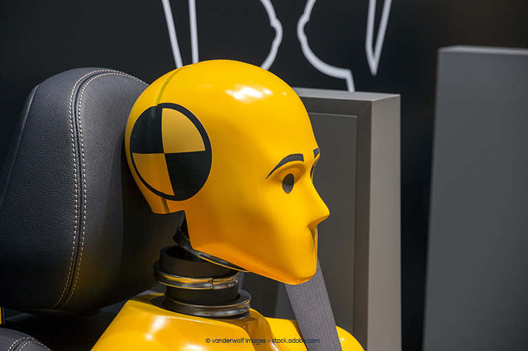 A yellow crash test dummy is seated in a car seat and strapped in with a seat belt.