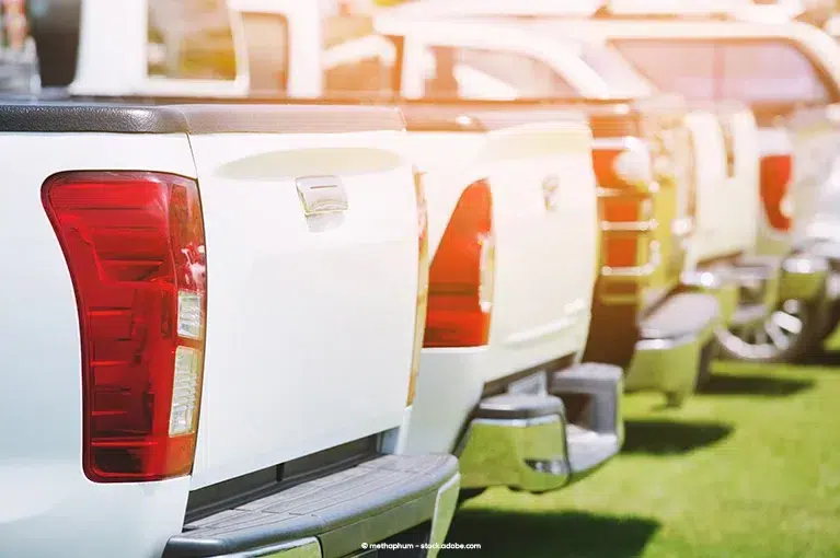 A fleet of white pickup trucks is parked on a faux-grass lot.