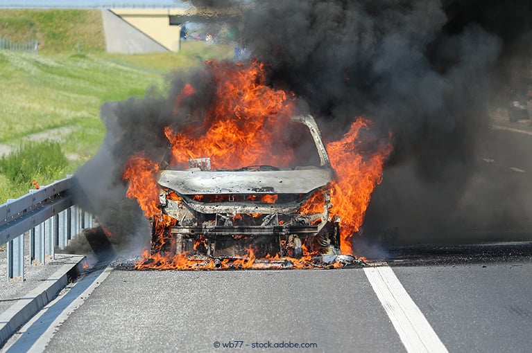 A vehicle is completely engulfed in flames and emits black smoke.