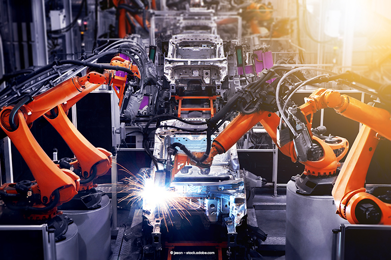 The interior of a vehicle factory. Orange mechanical tools weld and construct the vehicle body.