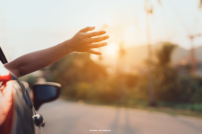 A passenger holds their hand outside of the vehicle window. The sunlight peaks through the passenger's fingers.