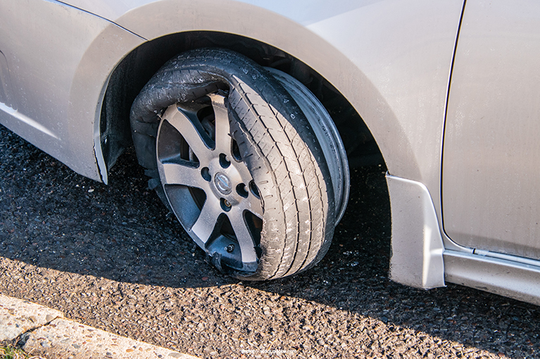 The rubber part of the tire is slipping off the rim of a parked car.