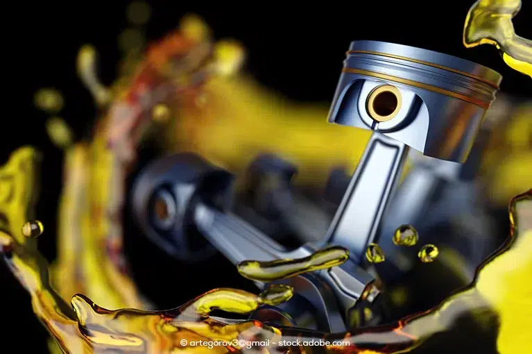 Engine pistons surrounded by yellow engine oil against a black background.