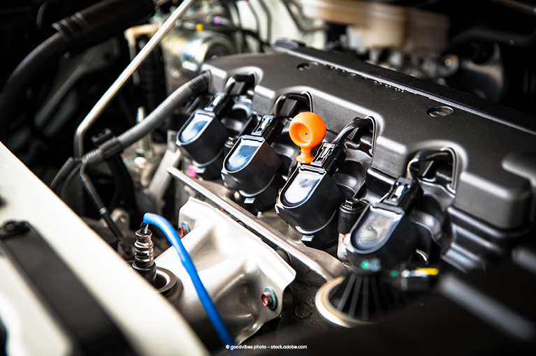 Four spark plugs are in the center of the frame. The picture itself is of the engine compartment under the hood.