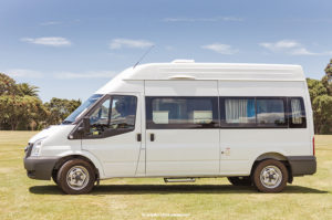 A white Ford Transit vehicle is parked on an empty, freshly shaven grass field.