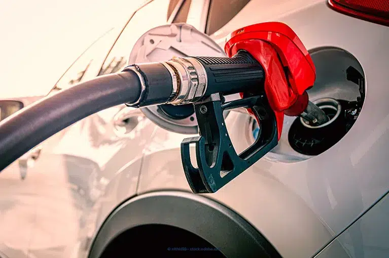 A fuel pump is depositing fuel into a white vehicle's fuel tank.