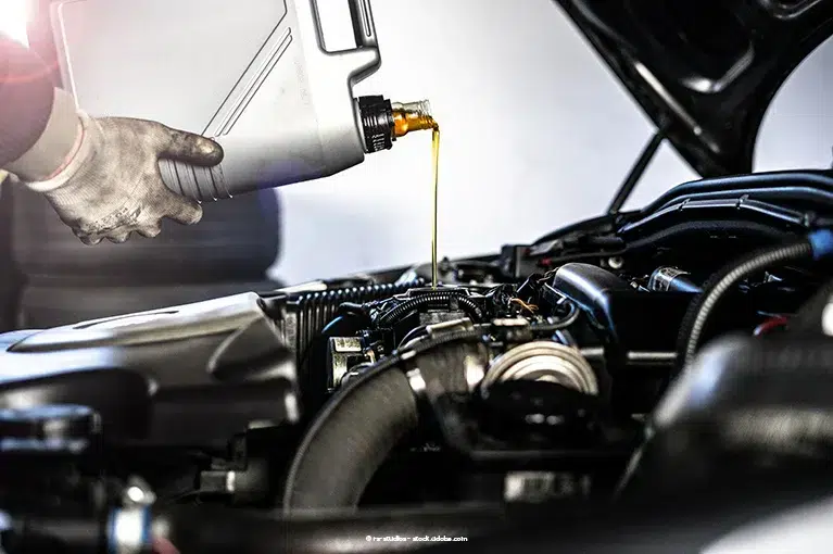 A mechanic with white gloves pours engine oil into an engine.