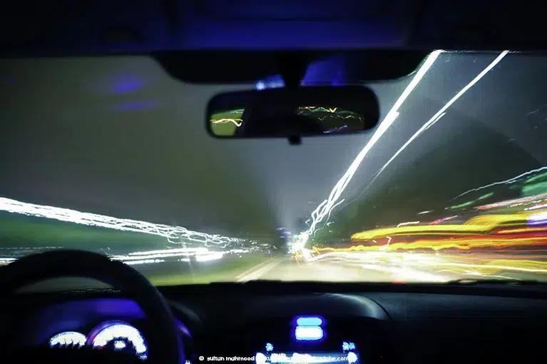 The light of streetlights, tail lights, headlights and buildings blur together in the background while the vehicle itself, from the driver's perspective, begins to shake.