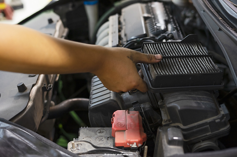 A person removes a filter from the compartment of her vehicle, under an open hood.