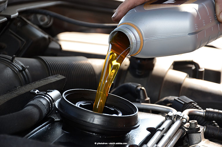 A gray bottle of yellow engine oil is poured directly into the engine.