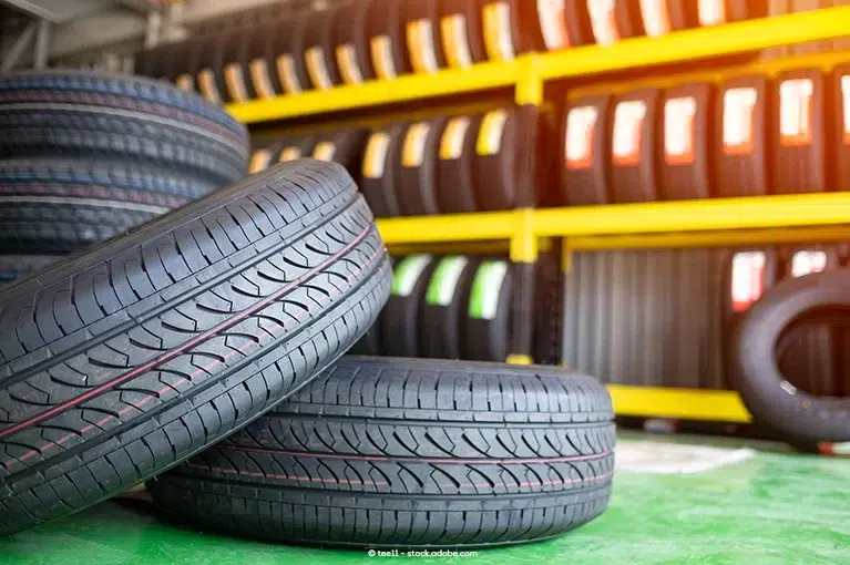 Two tires stacked on top of each other occupy the foreground of the image. In the background, a stack of tires rests to the left, and a shelf of tires lines the wall.