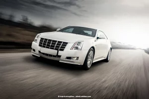 A Cadillac car speeds down an empty stretch of road, illuminated by a daytime overcast sky.