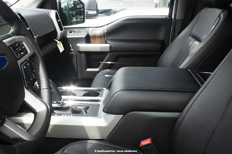 A shot of a vehicle interior from the view of the driver's side front window. The seats and compartments are upholstered in black leather, while the metallic components reflect bright light.