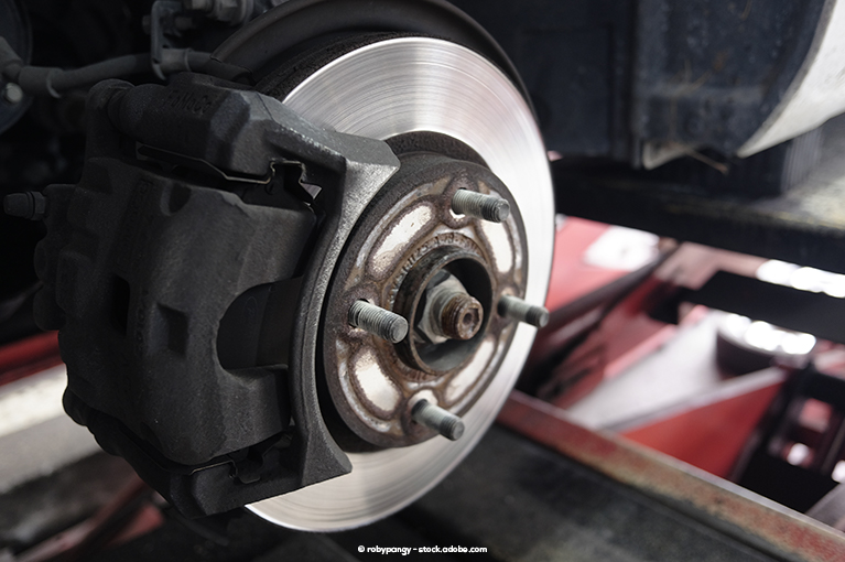 An exposed wheel and brake of a vehicle being suspended by a car lift.