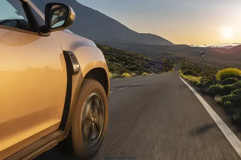 A Nissan Murano speeds down a single lane highway in a blooming desert.