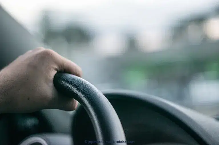 A close up of a hand gripping a steering wheel.