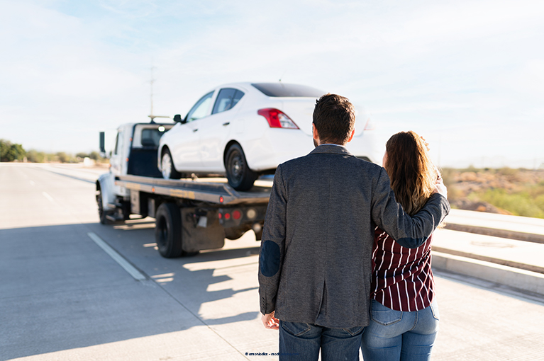 A couple watch as a white sedan is taken by a tow truck. If your Nissan Maxima has recurring problems that won’t go away or make it unsafe to drive, consider consulting with a lemon law attorney.
