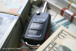 A key fob with the key sticking out is placed between stacks of cash.