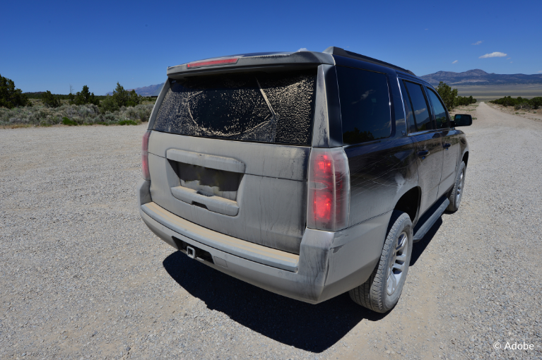 A Chevrolet Tahoe is parked on a gravel lot, Its trunk and rear window is covered in dirt.