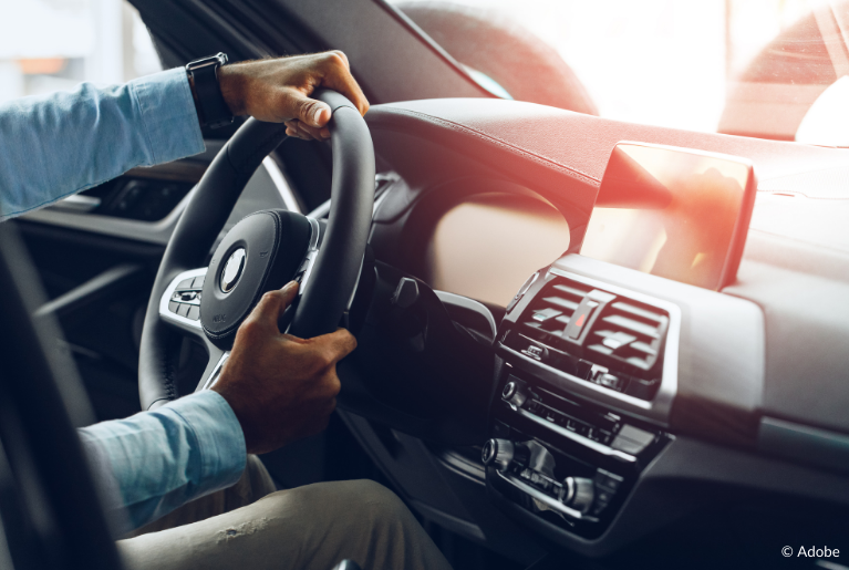 A view of a steering wheel, an blank dashboard and a radio infotainment system. A man sits in the driver's seat and steers the steering wheel to the right.