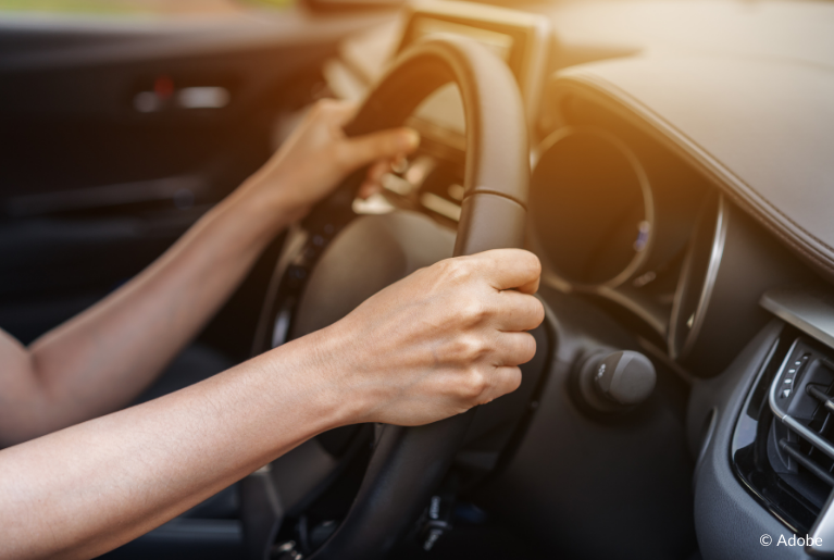 A close up of a steering wheel held by a female driver.