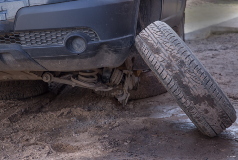 A tire is about to tip over and land sideways in front of a large vehicle, itself propped up by sideways, detached tires.