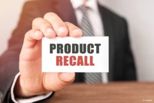 A man in a suit holds up an index card that says "Product Recall."