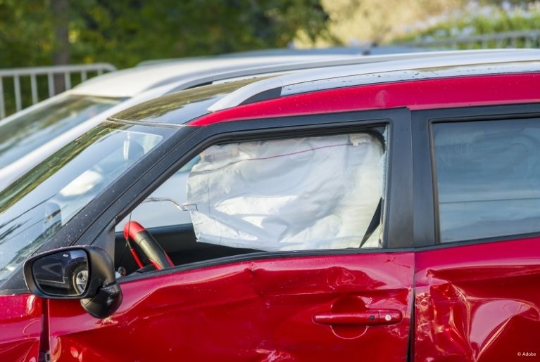 A red vehicle has its driver side doors dented. Its side airbag deployed and deflated.