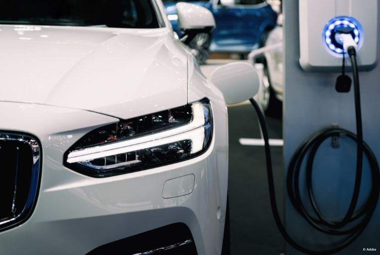 A white Chevy bolt is parked in an indoor parking structure. It is plugged in and charged.