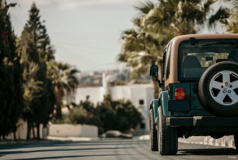 A green Jeep with a beige roof parked on an empty downhill street.