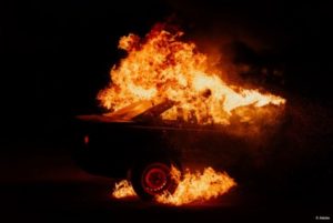 A fire engulfs a car. It is nighttime. The fire illuminates nothing around it.