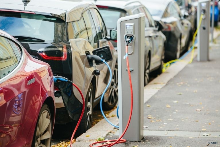 Several cars are parked along EV charging stations built into the sidewalk.