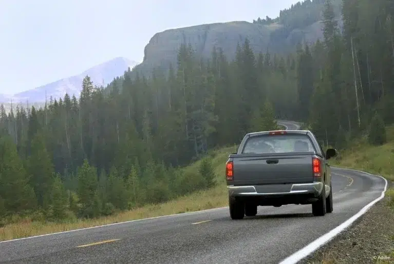 A grey Dodge Ram pickup truck is driving along a road in the forested mountains.