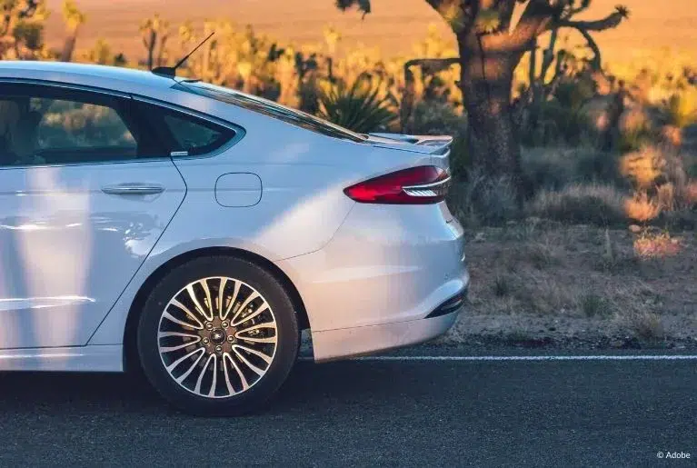 The rear of a white Nissan Rogue parked on the side of the street in a desert.