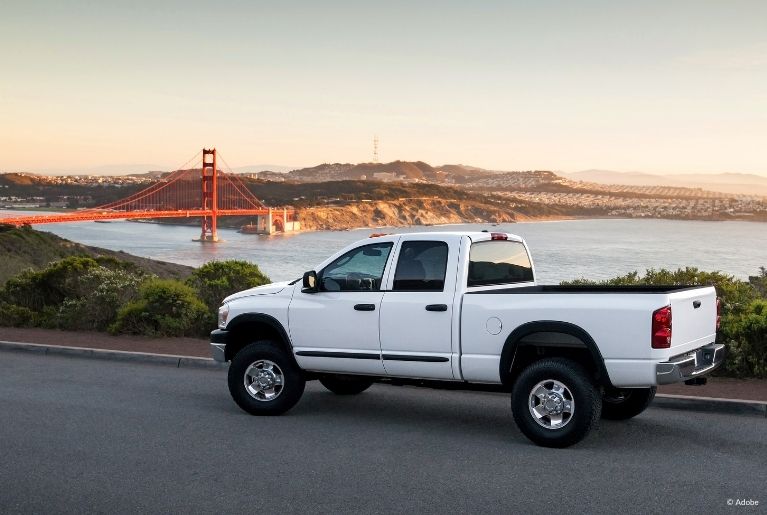 A white RAM pickup truck is parked on an empty street in front of the Golden Gate Bridge.