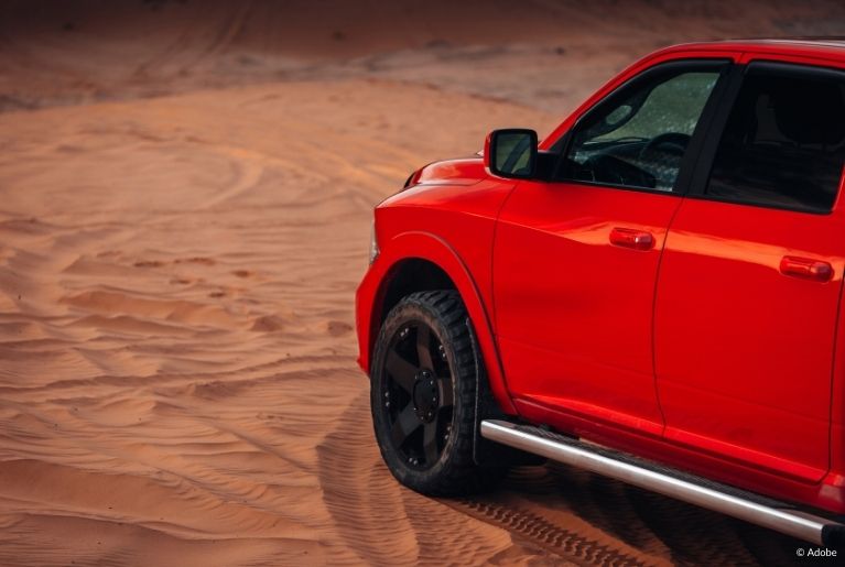 A red RAM truck is parked in a sandy desert.