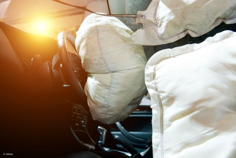 The driver's frontal and side airbags have deployed. Sunset peaks through the windshield.