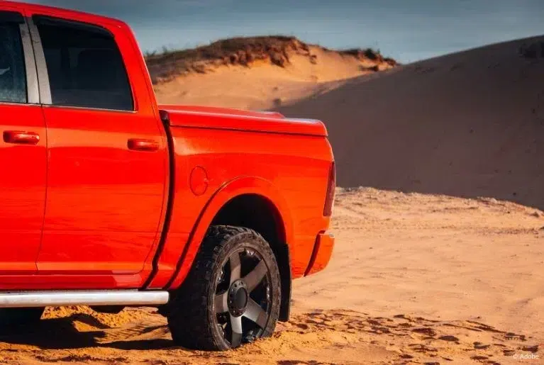 The rear half of a red Ram pickup truck parked in a sandy desert.