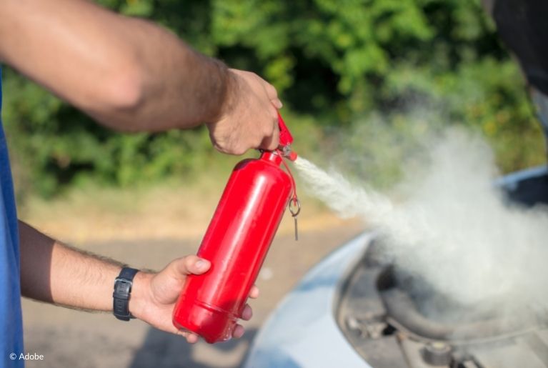 A man uses a fire extinguisher on the engine compartment of his car.