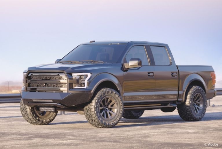 A black Ford pickup truck is parked on an empty lot with a freeway guardrail.