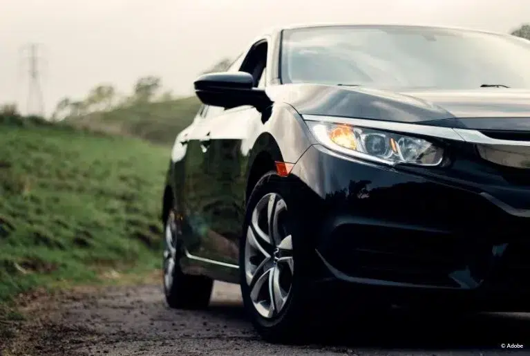 The passenger side of a black Honda sedan is in frame, parked on the side of a dirt road.