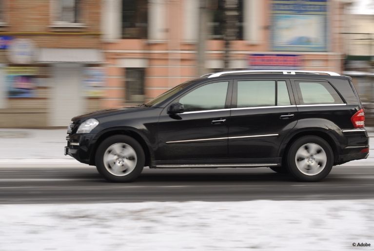 A black Nissan Murano SUV speeds on a road. Behind the road is a snow-covered sidewalk in front of various businesses.