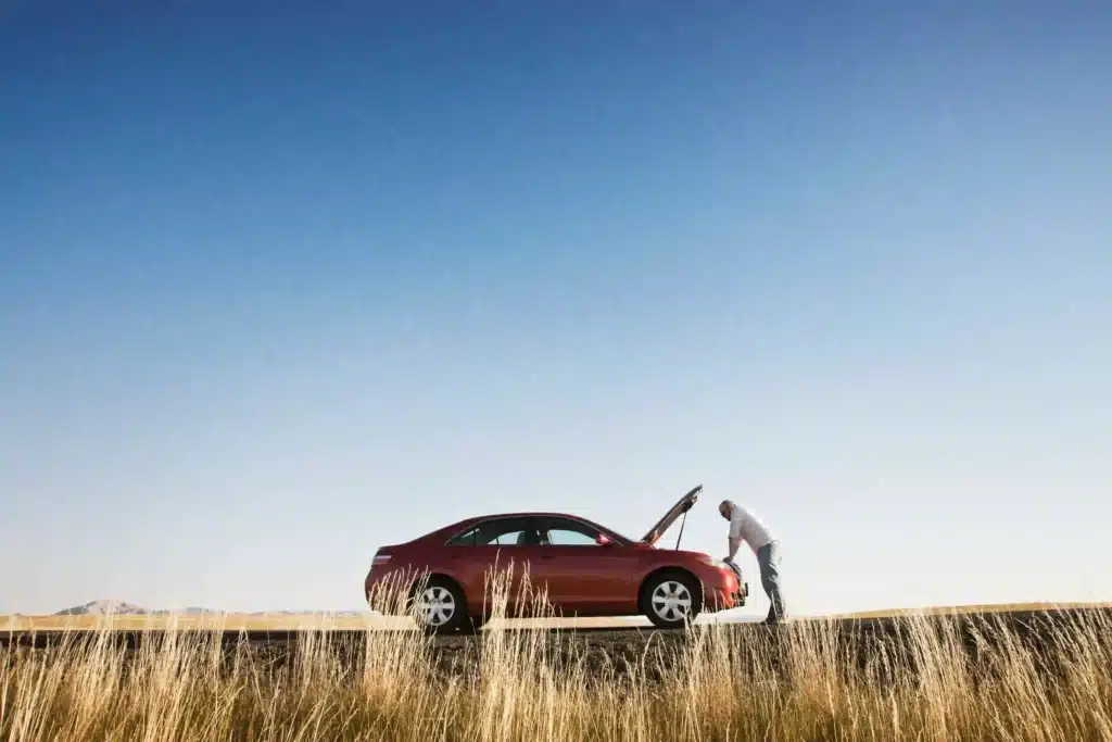 Man leaning against car with hood open on side of road